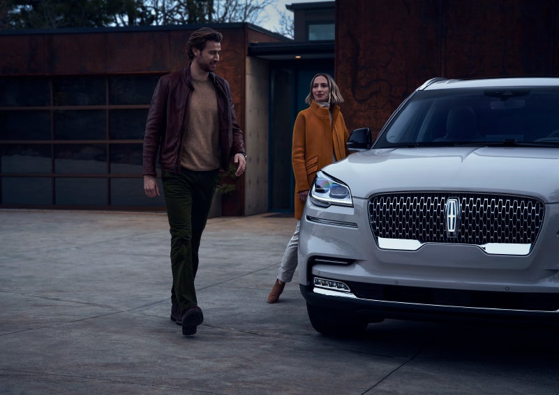 A man and a woman approaching a 2024 Lincoln Aviator® SUV, which illuminates certain lights when they are close | Preston Lincoln in Hurlock MD